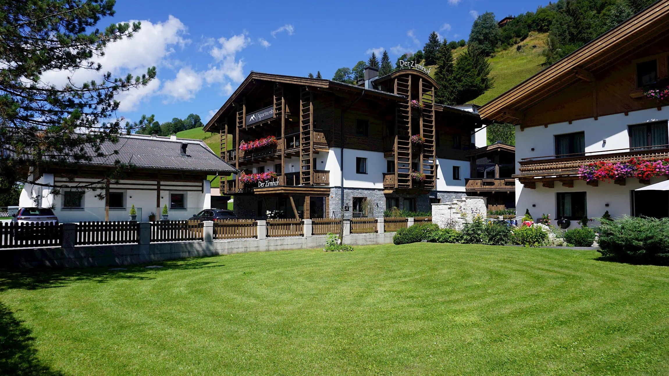 Aussenansicht Zirmhof im Sommer. Im Vordergrund grüne Wiese, im Hintergrund Berge.