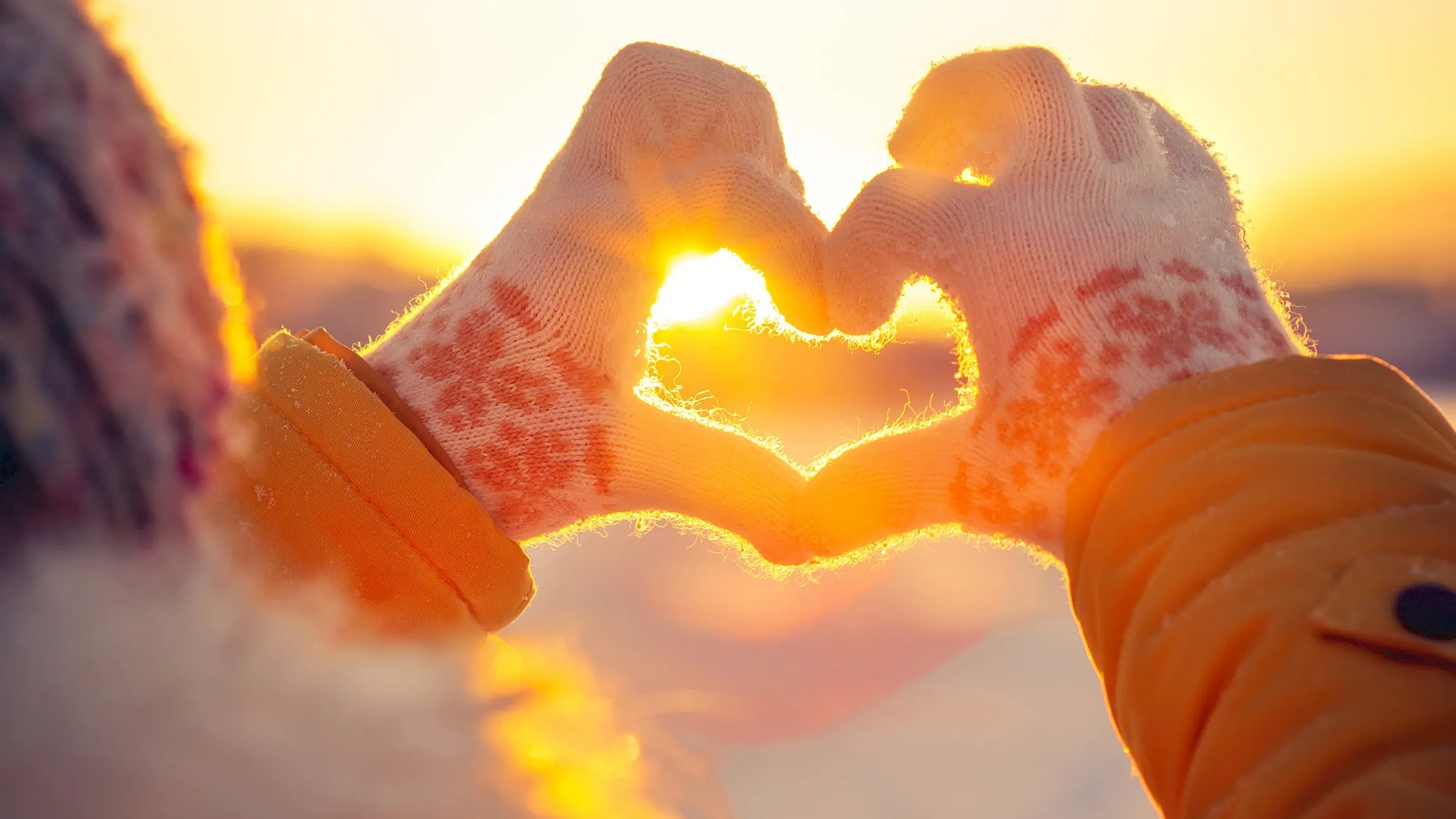 Hands forming a heart, in the background sunset and winter landscape. Winter offers that make you happy at the Zirmhof