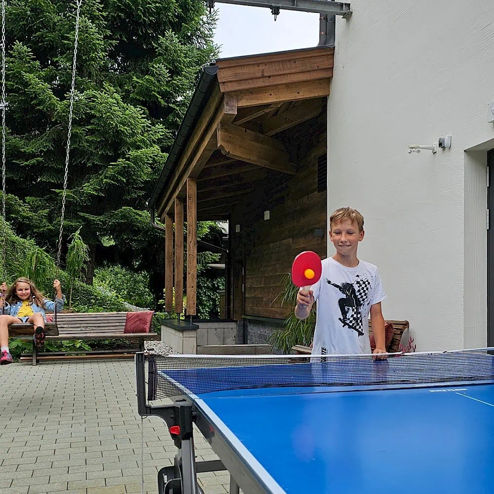 Junge spielt Tischtennis und Mädchen schaukelt hinterm Zirmhof