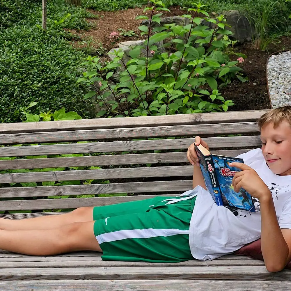 Boy lies on the bench and reads a book | Zirmhof