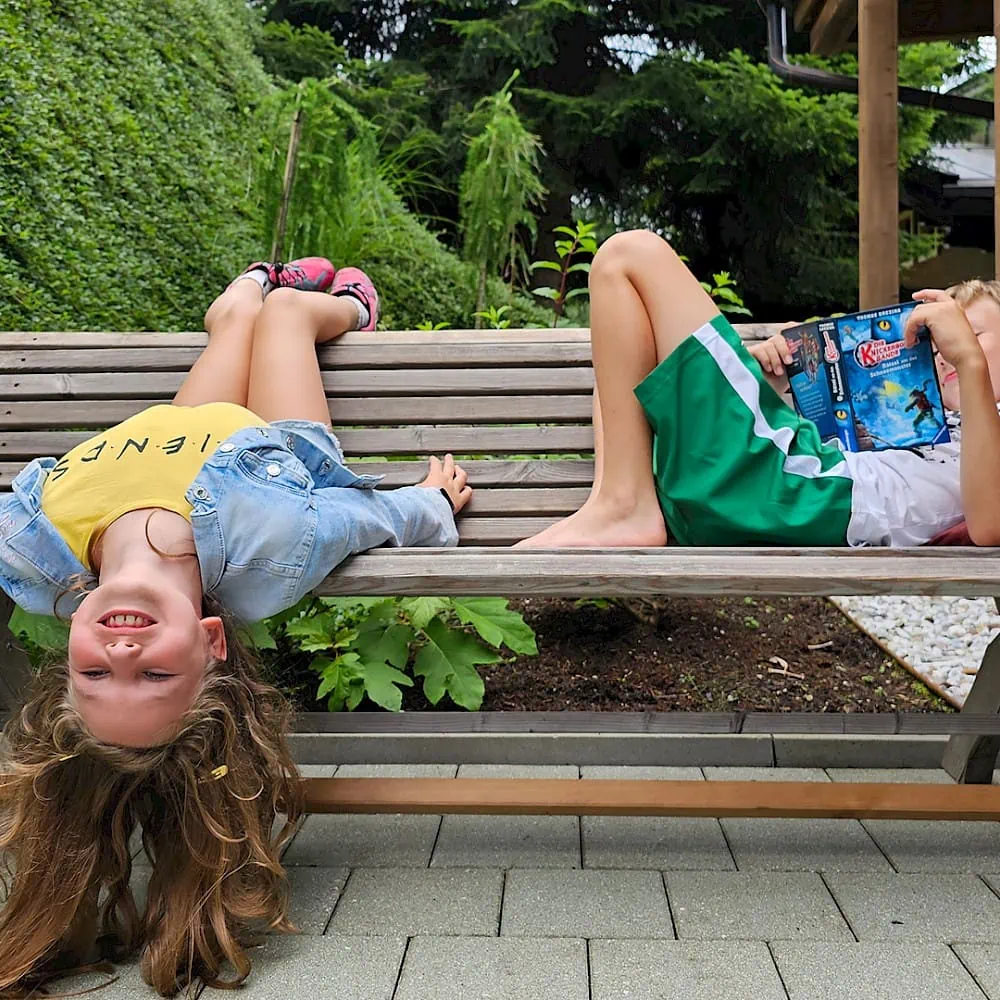 Girl does gymnastics on the bench, boy reads a book