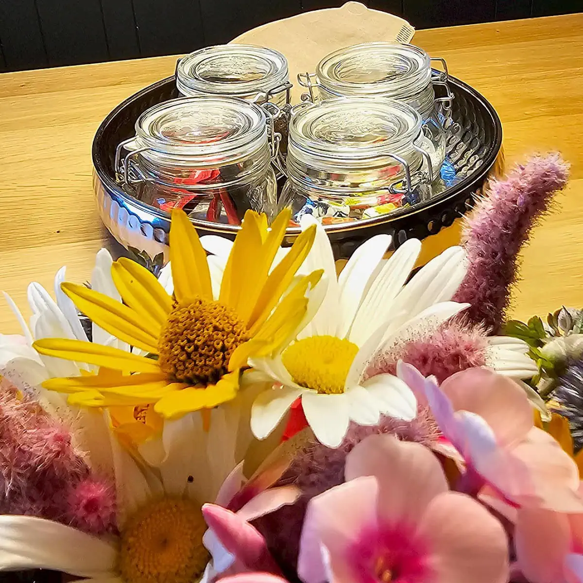 Esstisch mit Willkommensgeschenk bestehend aus Kaffee, Tee und etwas Süßem. Auf dem Tisch steht eine Vase mit Blumen.